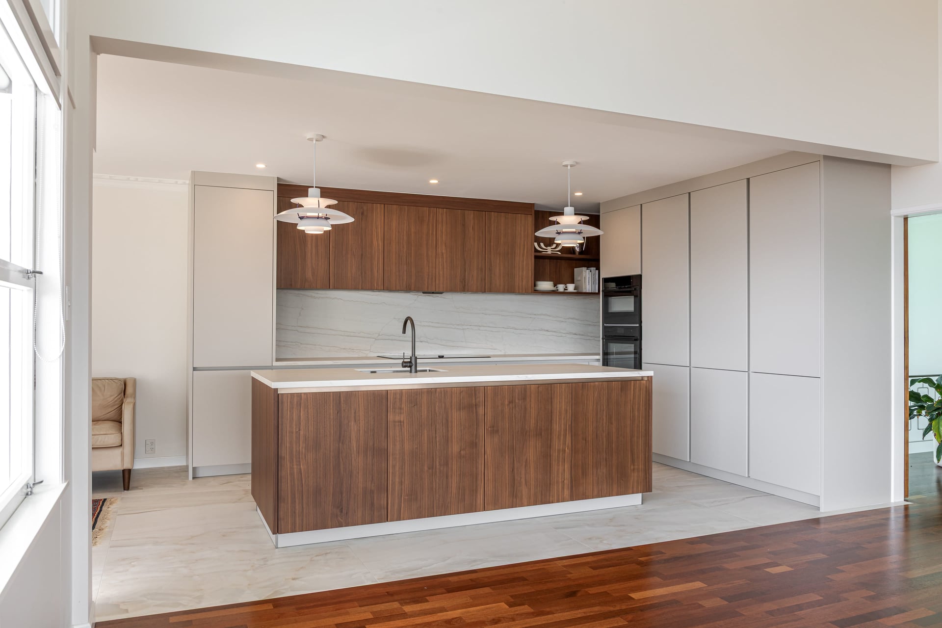 A full-height cabinet wall keeps storage behind pale handleless doors, with the island in front.