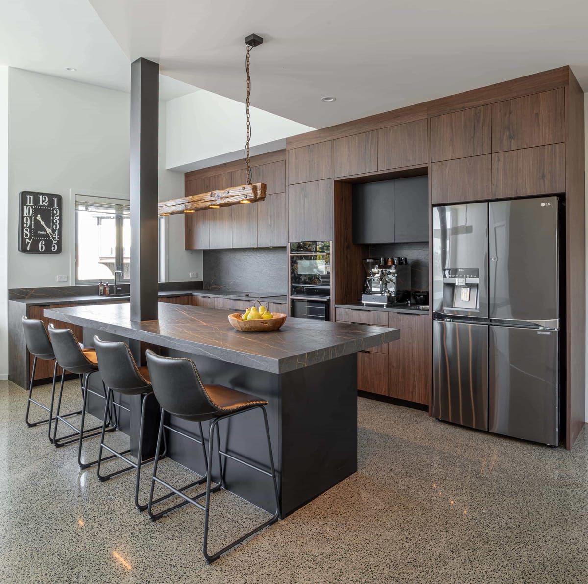 Dark stone island with four stools, and a recessed coffee niche beside the fridge