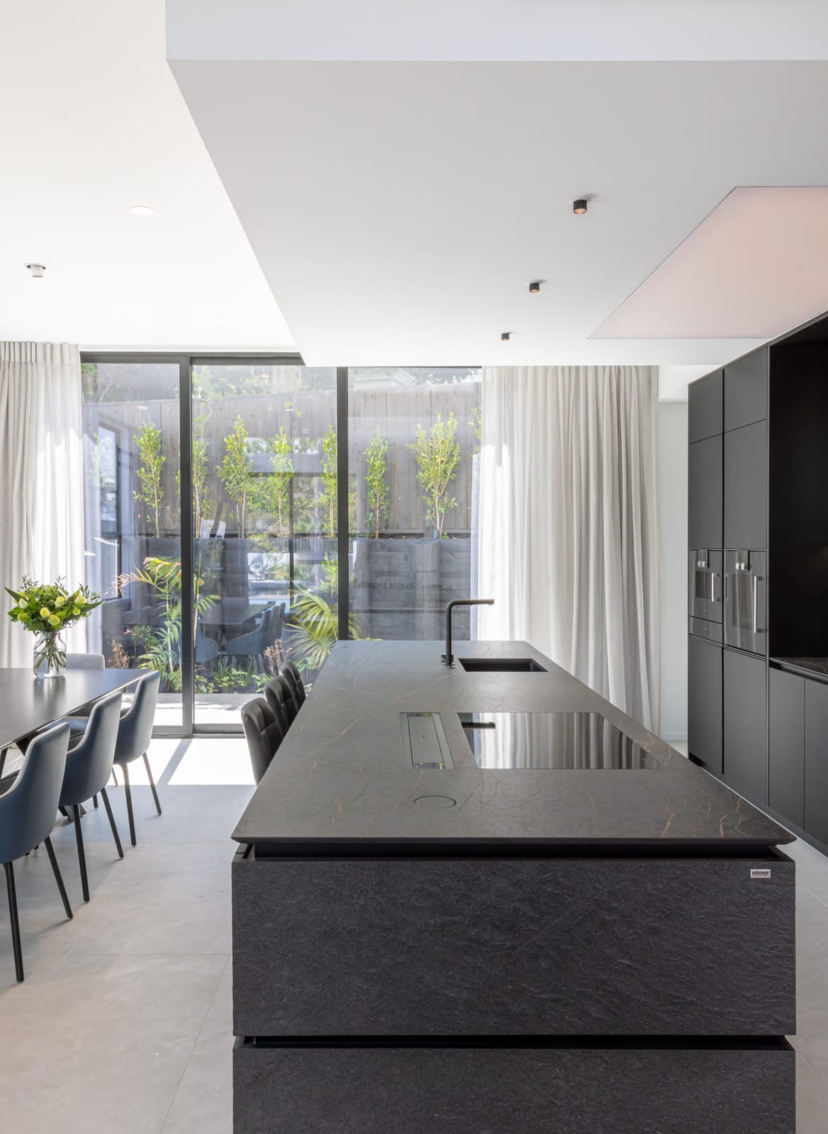 Dark stone island with a sink and flush cooktop, and a clear walkway to the dining table