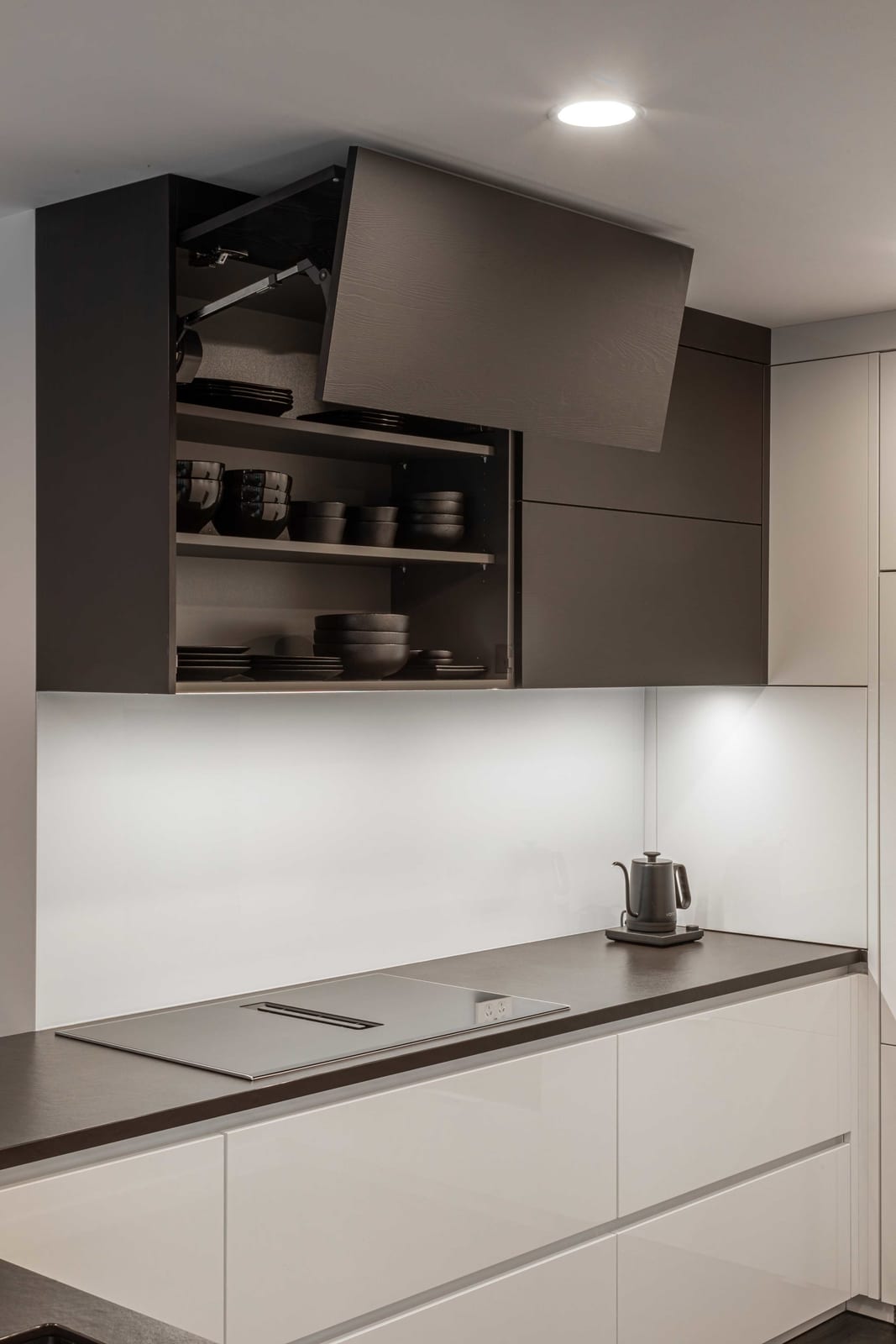 Lift-up wall cabinet door raised over the cooktop to reveal shelves of dark crockery