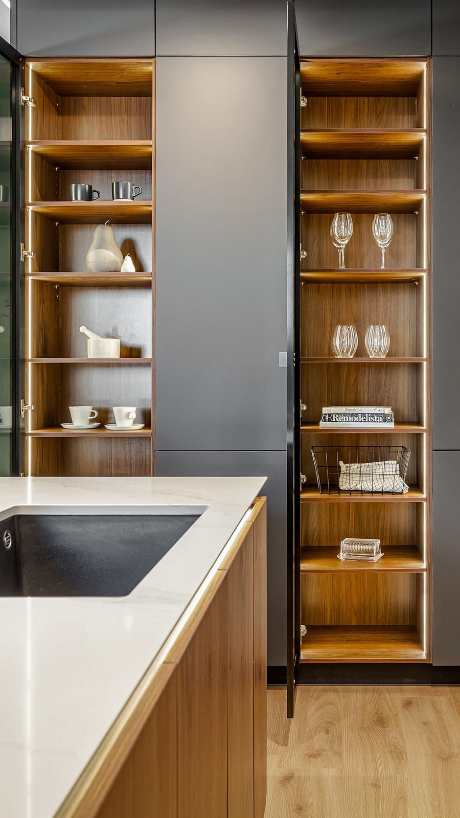 Two tall cabinets open to reveal lit timber-look shelves of cups and glassware