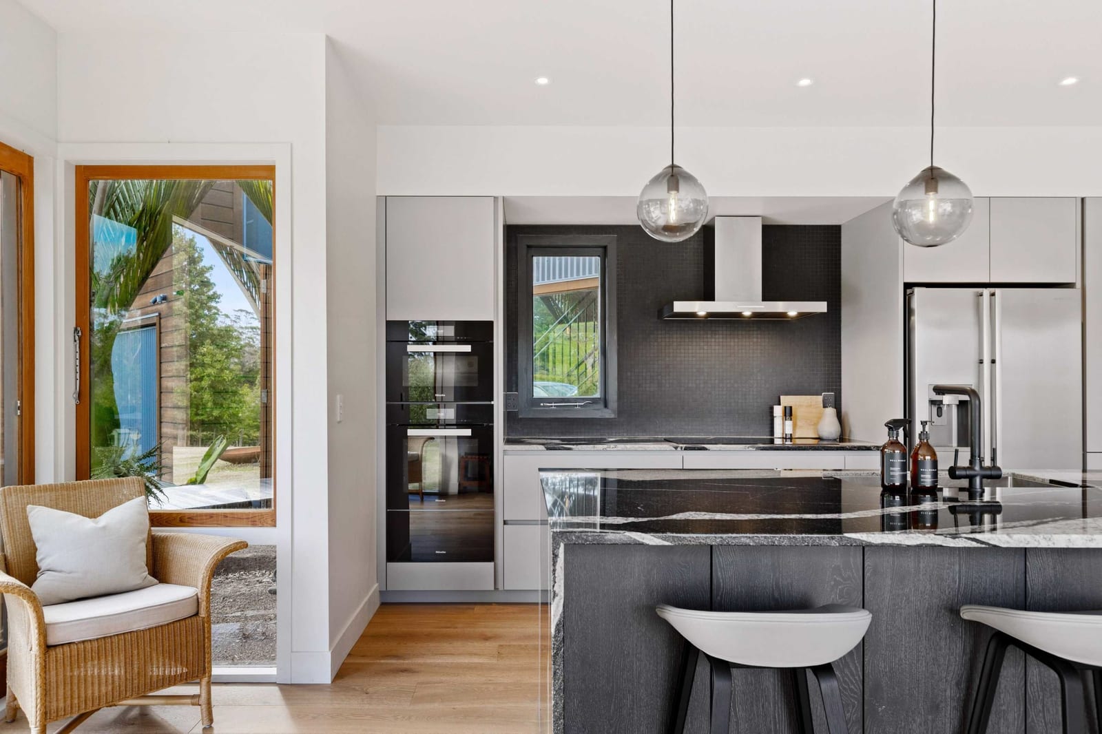 Oven tower and small black-framed window set into a dark mosaic splashback, beside a garden door