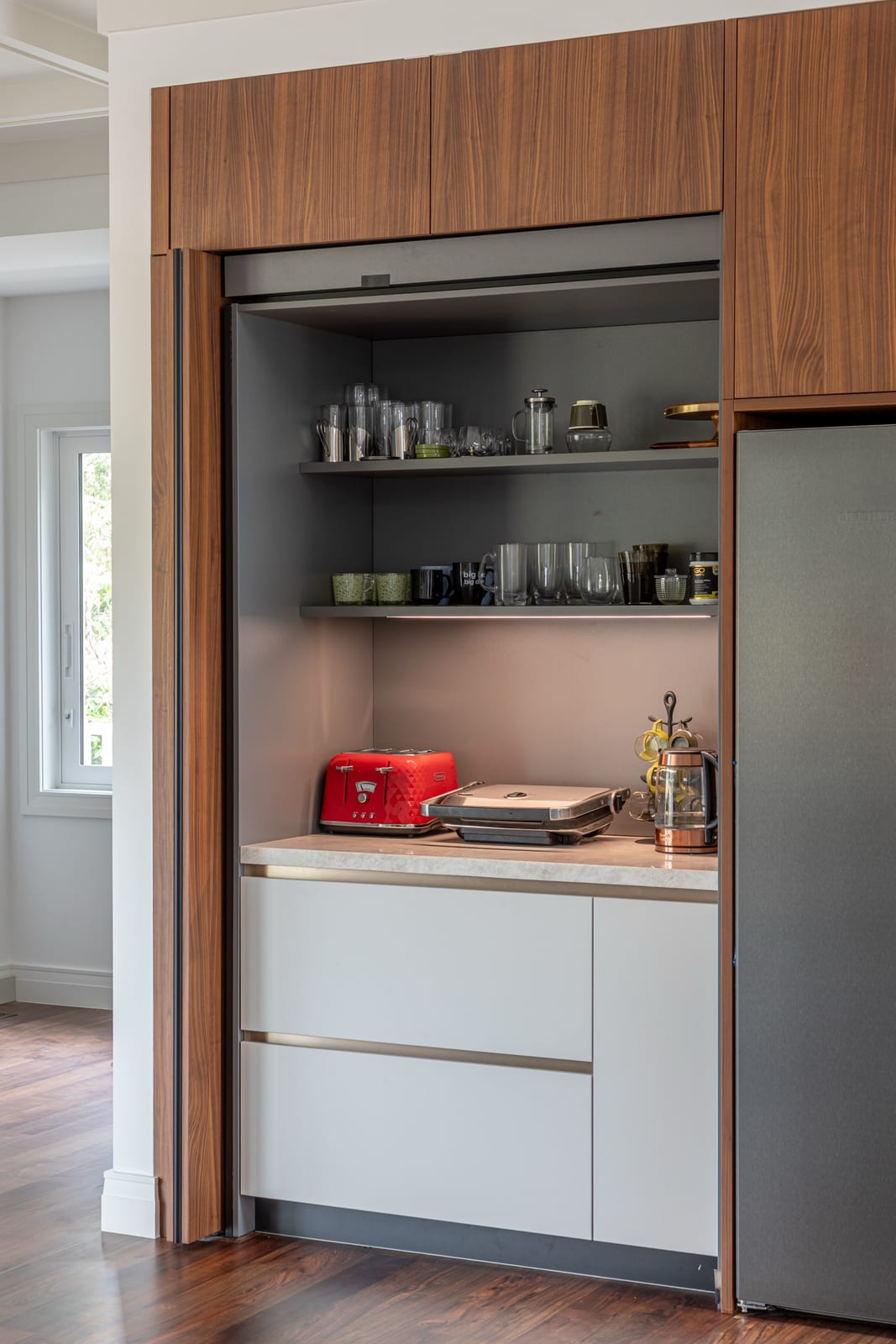 Pocket doors fully open revealing an appliance cupboard with toaster, kettle and glassware