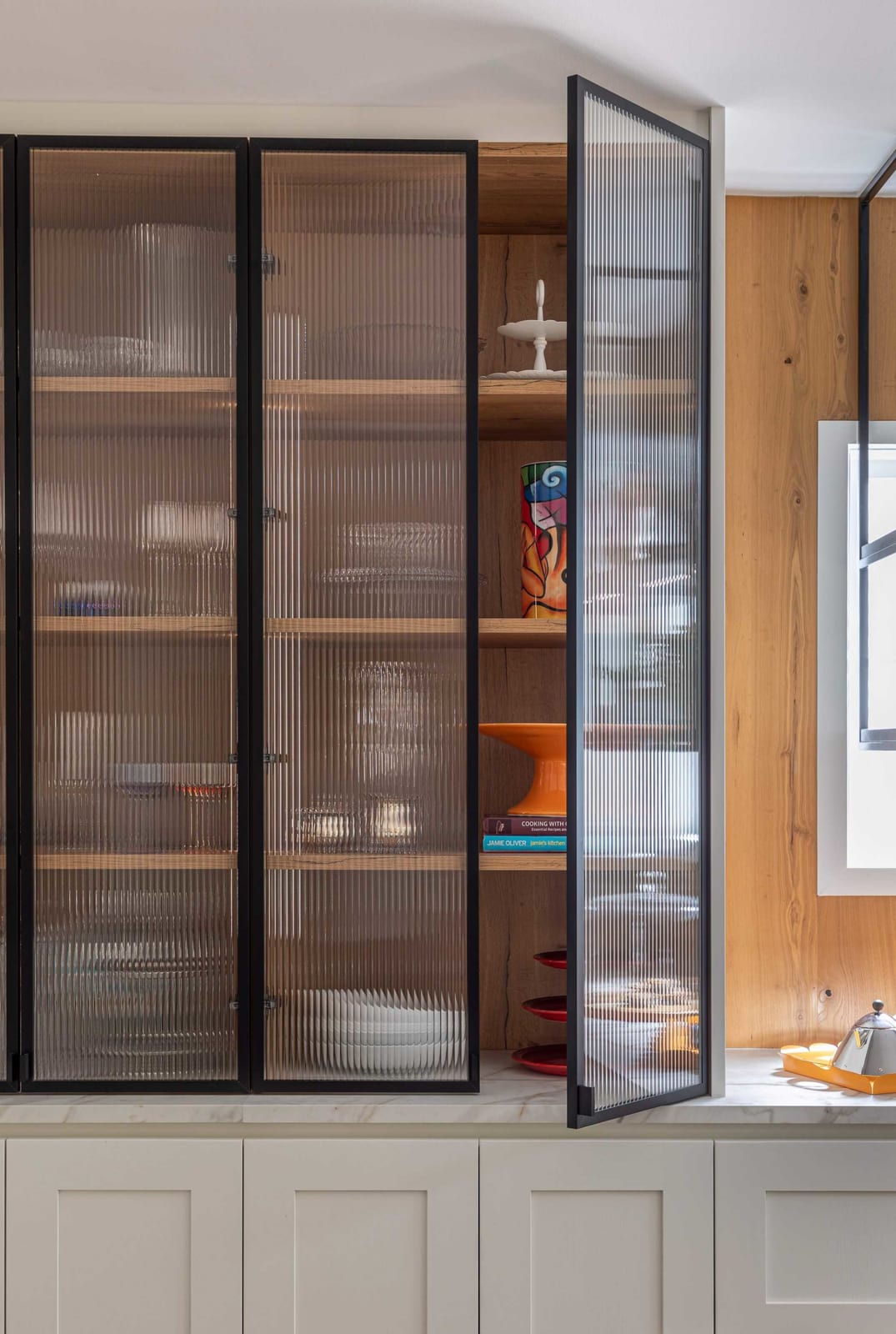 Black-framed ribbed-glass display cabinets, one door open to timber shelves of serveware