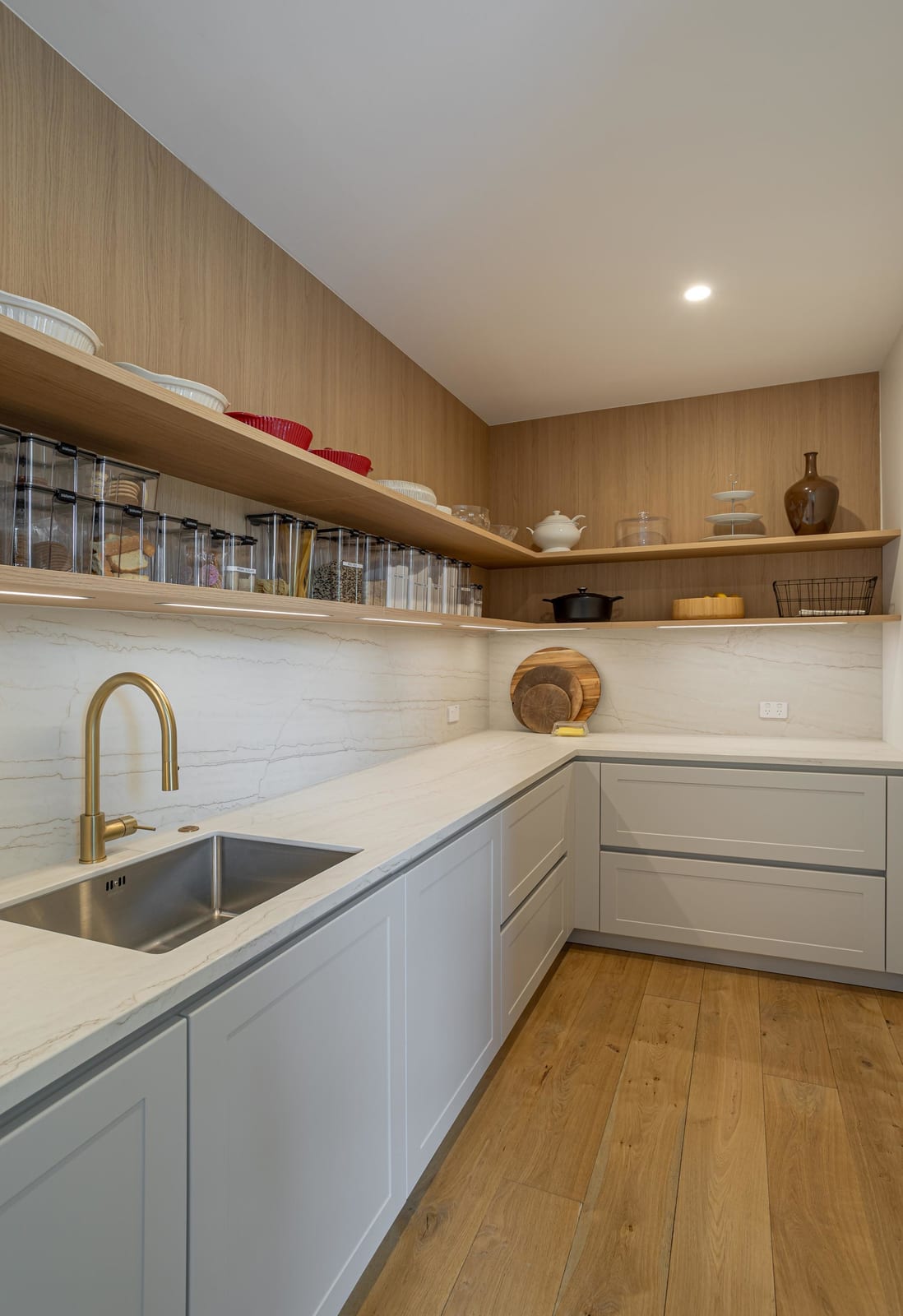 Scullery with long timber-look shelves of clear canisters over a veined stone benchtop