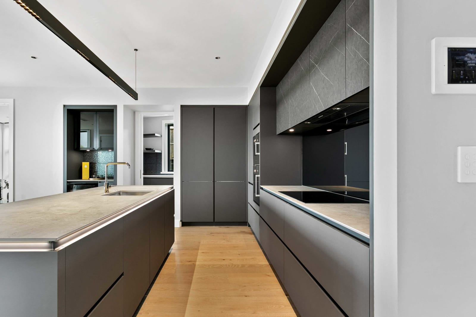 Timber-floored walkway between a charcoal island with sink and a handleless cooking run